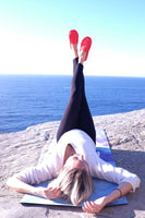 Vrouw met loafers tijdens yoga op de rotsen in de zon met uitzicht op de zee